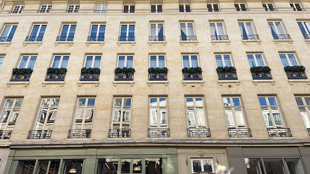Un edificio de varios pisos con arquitectura clásica, con ventanas y balcones uniformemente distribuidos y plantas.