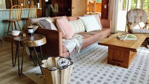 Un salon chaleureux avec un canapé en cuir marron, une table basse en bois, un panier en osier et une petite table ronde sur laquelle est posée une bougie.