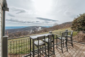 A deck with a table and chairs overlooking a mountainous landscape.