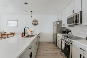 Eine moderne Küche mit weißen Schränken, Edelstahlgeräten und einem Holztisch.