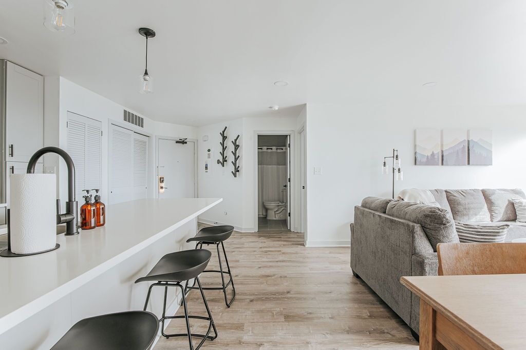 A modern kitchen with a white countertop, bar stools, and a wooden dining table.