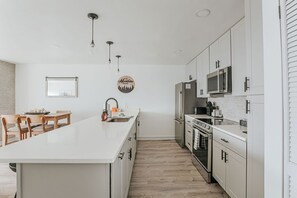 A modern kitchen with white cabinetry, a central island, and a dining area with wooden chairs. - Mountain View Vista: Resort Condo w/ Views (Wintergreen Resort)