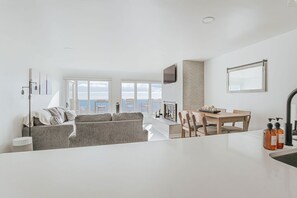A modern living room with a sofa, a dining table with chairs, and a kitchen area with a sink and countertop.