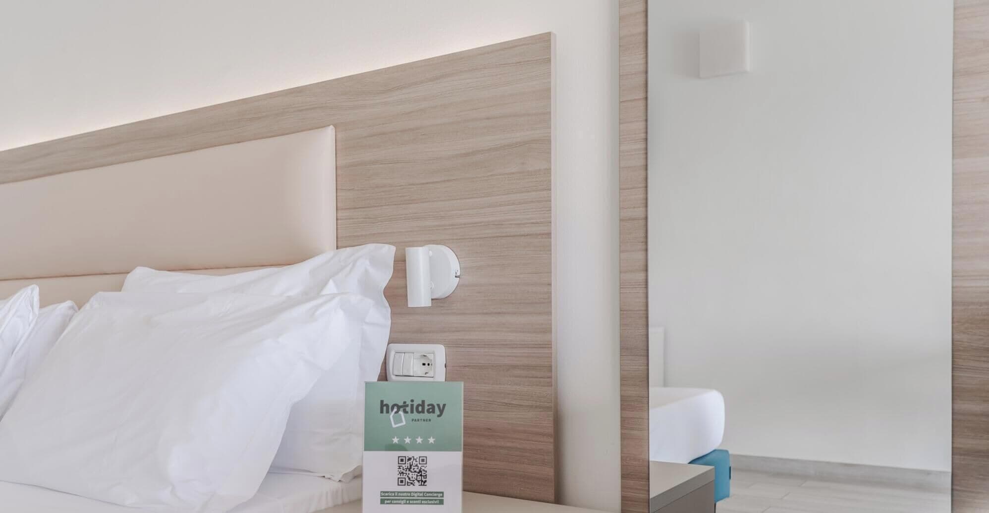 Een hotelkamer met een bed, nachtkastje en een wandlamp.