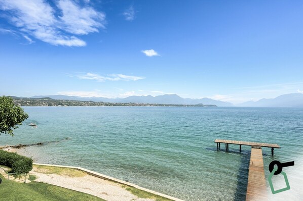 A clear lake with a wooden dock extending into the water, surrounded by mountains and a clear sky. - HOTIDAY Apartments Desenzano (Desenzano del Garda)