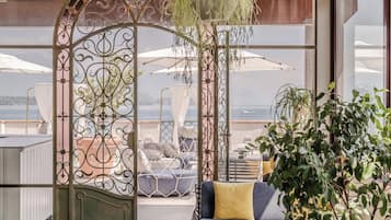 Ein modernes Interieur mit Meerblick, bestehend aus einem blauen Sofa mit gelben Kissen, einem großen Kübelpflanze und einem dekorativen Metallgitter.