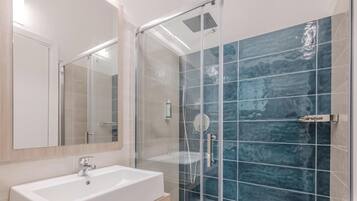 A modern bathroom with a white sink, a glass shower enclosure, and a large mirror.