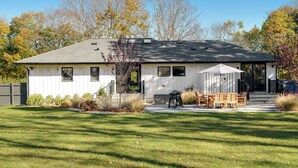 A single-story house with a covered patio, a barbecue grill, and a small garden area. - Spacious and Modern North Fork Home Close to Multiple Wineries, Perfect for... (Cutchogue)