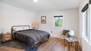 A bedroom with a bed, bedside table, lamp, and window with a view. - Spacious and Modern North Fork Home Close to Multiple Wineries, Perfect for... (Cutchogue)