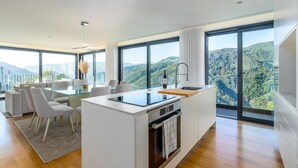 A modern kitchen with a central island, large windows, and a dining area with chairs.