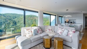 A modern living room with a large sectional sofa, a glass dining table, and a kitchen area.