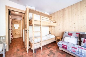 A room with a bunk bed, a sofa with patterned cushions, a small wooden table, and a door leading to another room.