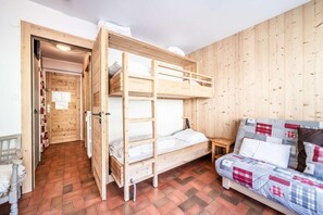 A room with a bunk bed, a sofa with patterned cushions, a small wooden table, and a door leading to another room. - Resort center, 2nd floor, balcony, tv, 30m², Morzine (Morzine)