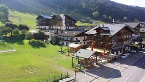 Un hotel de estilo chalé tradicional, con varias construcciones, una zona de estacionamiento y un paisaje verde con árboles y colinas al fondo.