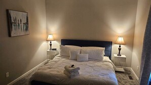 Ein ordentlich bezogenes Bett mit weißen Leinen und Kissen, zwei Nachttischlampen, ein Nachttisch und ein Gemälde an der Wand.