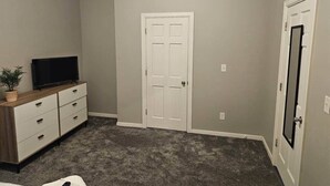 Ein Zimmer mit einer weißen Tür, einem Fernseher auf einer Holzkassette und einem Teppichboden.