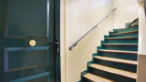 Un escalier avec des marches en bois et une rampe métallique, menant à une porte dotée d’une poignée de porte en laiton.
