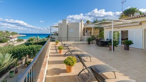 Terraza en la azotea con vistas al mar, mobiliario exterior y plantas en macetas.