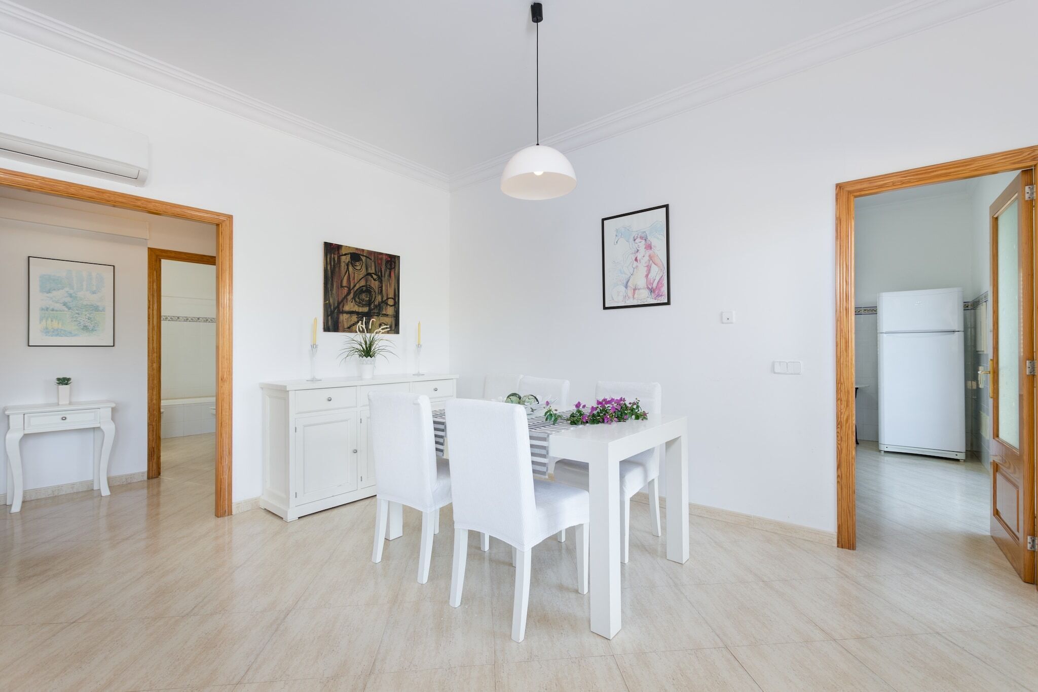 A modern kitchen with white cabinetry, a dining table with chairs, and a pendant light.