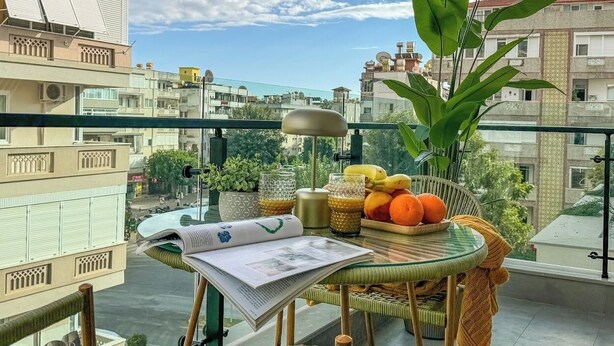 Un balcón con una mesa dispuesta para el desayuno, con frutas y un periódico.