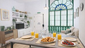 Colazione con croissant, frutta e succo d'arancia su un tavolo in una stanza con una finestra verde, pareti bianche e una porta bianca con la scritta 'SALIDA'.