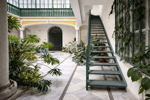 Un escalier dans un bâtiment dont le sol est recouvert de carreaux, entouré de plantes en pot.