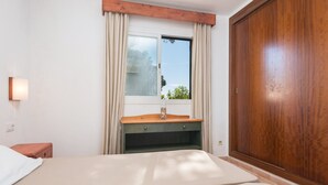 A bedroom with a bed, a wooden nightstand, a dresser, a window with curtains, and a wooden wardrobe. - Burgit - Apartment In Es Cap Des Moro. Free Wifi (Porto Petro, Illes Balears)