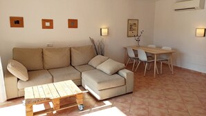 A living room with a sectional sofa, a wooden coffee table, a dining table with chairs, and wall-mounted lighting. - Burgit - Apartment In Es Cap Des Moro. Free Wifi (Porto Petro, Illes Balears)