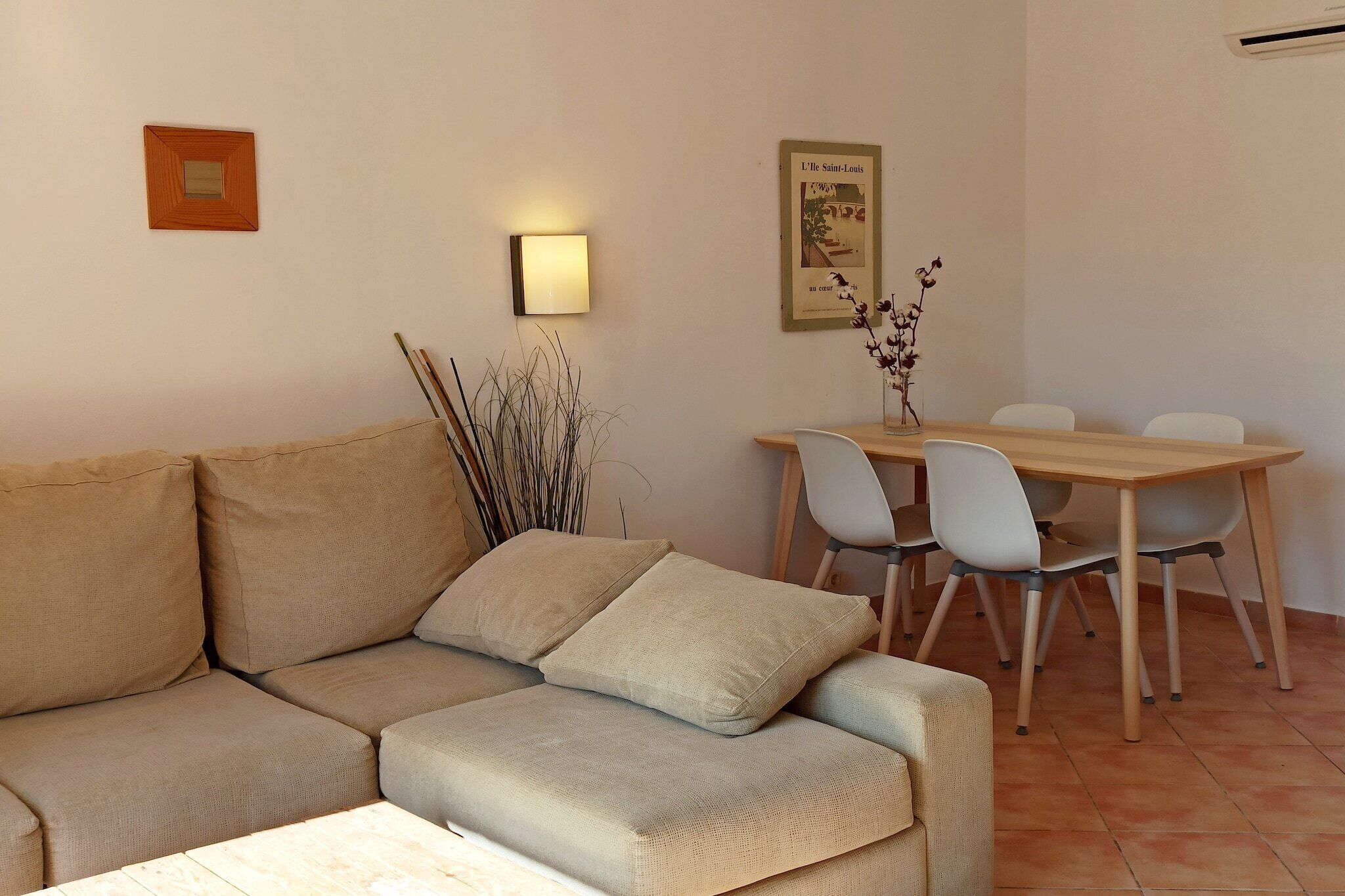 Una sala de estar con un sofá color beige, una mesa de comedor con sillas y una lámpara fijada a la pared.