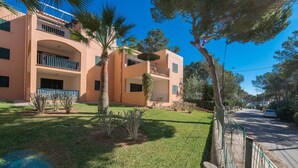 A two-story building with balconies, a well-maintained lawn, and a clear sky. - Burgit - Apartment In Es Cap Des Moro. Free Wifi (Porto Petro, Illes Balears)