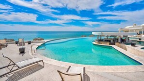 Un espace piscine avec des chaises longues, un bar et une vue sur l’océan.