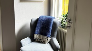 A grey armchair with a blue blanket, a framed picture on the wall, and a door leading to a room with a radiator and a window.