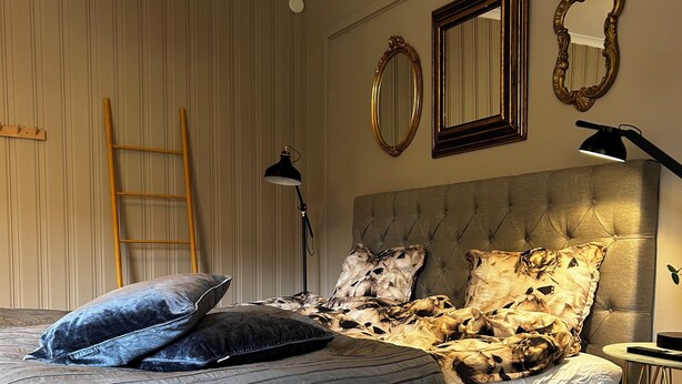 A bedroom with a large bed, a wooden ladder, two wall-mounted mirrors, and a bedside table with a lamp.