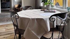 A dining area with a table set for two, a potted plant, and a framed picture on the wall.