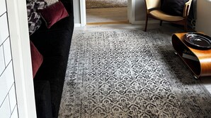 A modern living room with a patterned rug, a sofa, a chair, and a bed with a tufted headboard.