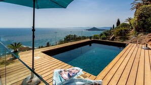 A private pool with a wooden deck, a large umbrella, and a scenic ocean view.