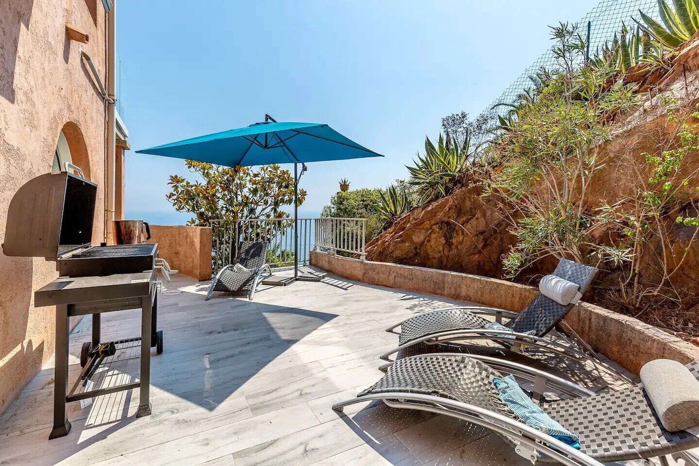 A patio with outdoor seating, a grill, and a view of the sea.