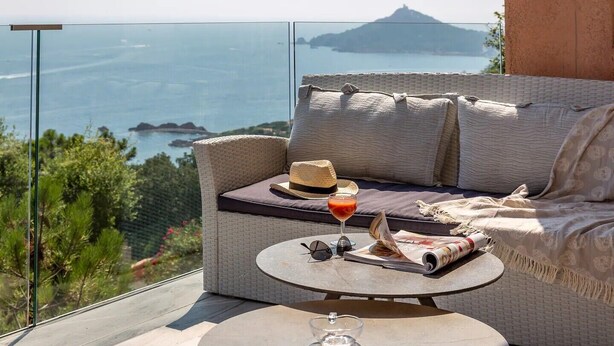 A balcony with a wicker sofa, a small round table, and a drink.