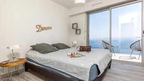A bedroom with a bed, bedside table, lamp, and a view of the balcony.
