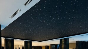 En moderne indendørs swimmingpool med stjernehimmel, loungeområder og en person, der bruger en mobil enhed.