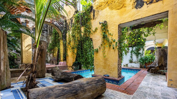 A courtyard with a pool, wooden logs, and tropical plants. - Alta Gastelbondo (Cartagena de Indias)