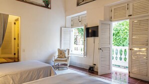 A hotel room with two beds, a ceiling fan, a TV, and a large window with shutters. - Alta Gastelbondo (Cartagena de Indias)