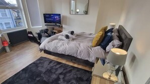 A modern bedroom with a bed, a TV, a heater, and a window with a view of buildings.