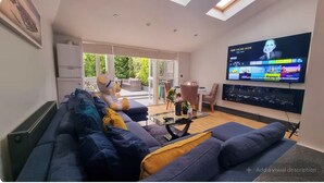 A modern living room with a large flat-screen TV, a sofa, a coffee table, and a sliding glass door leading to a patio.