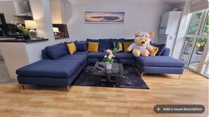 A modern living room with a blue sectional sofa, a glass coffee table, and a teddy bear.