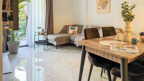 A modern living room with a wooden dining table, a sofa, and a coffee table. There is a bookshelf and a potted plant.