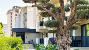 A modern building with a central staircase, surrounded by lush greenery and a large tree.