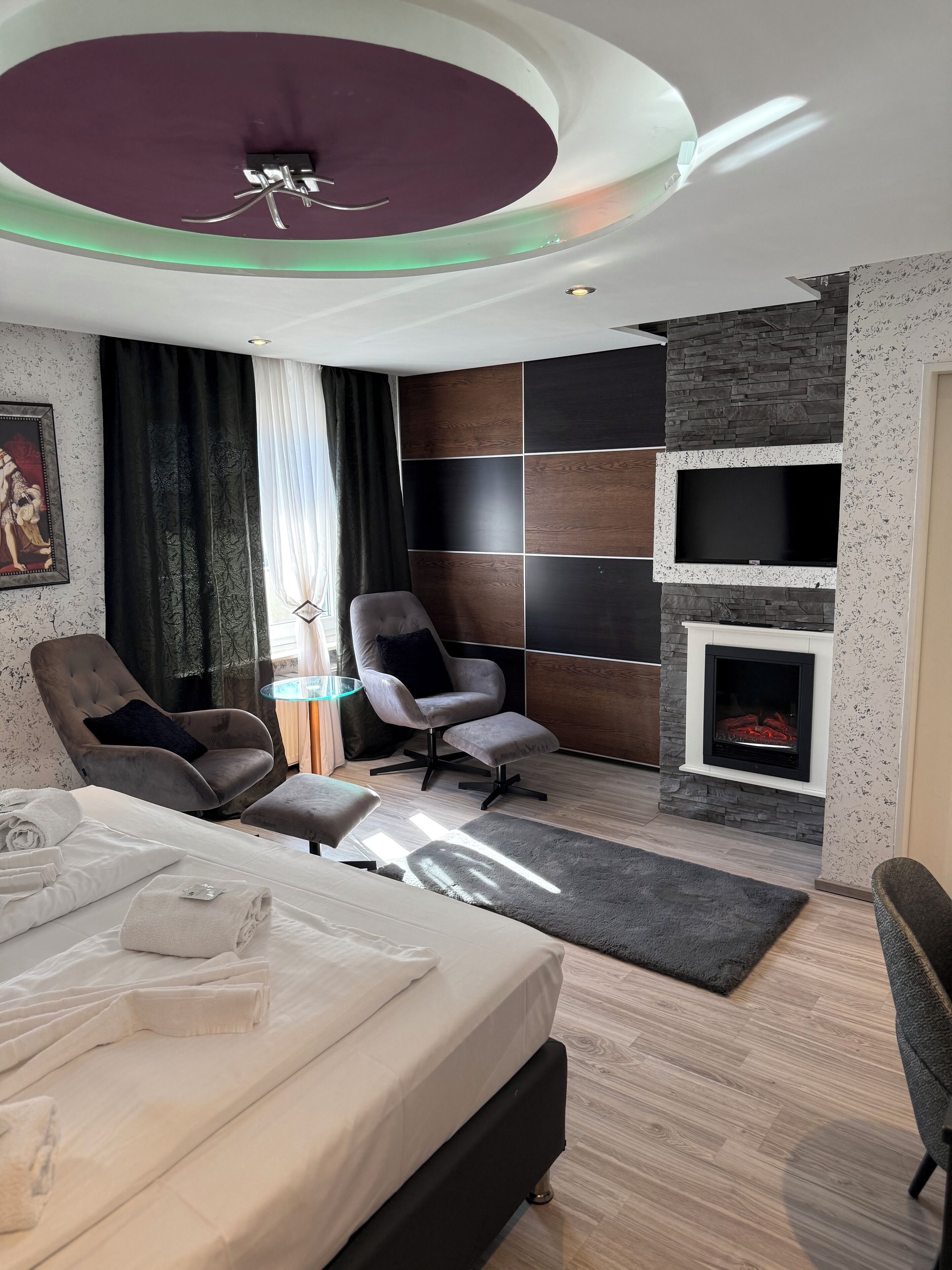 Habitació d'hotel moderna amb un llit, dues butaques, una llar de foc i una làmpada al sostre.