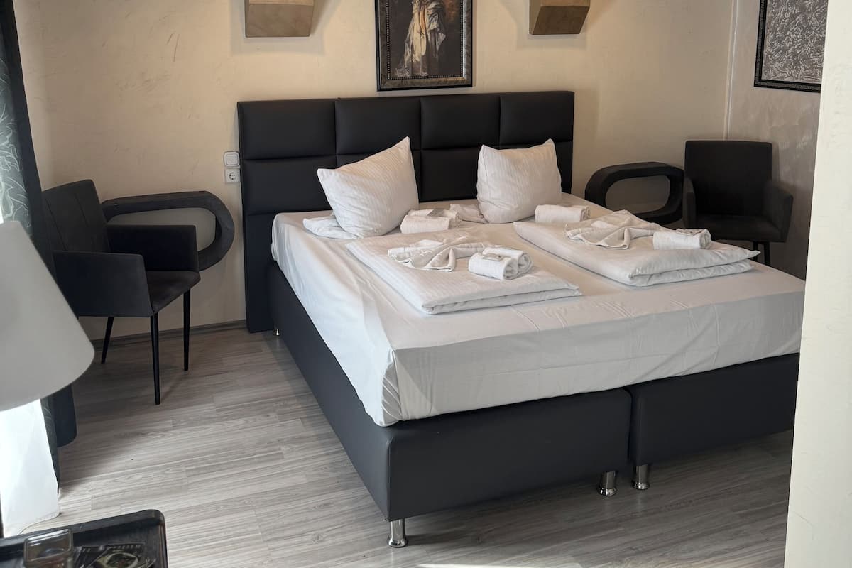 A modern hotel room with a large bed, two armchairs, a desk, and a framed artwork on the wall.