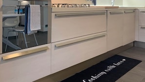 A modern kitchen with white cabinets, a stainless steel range hood, and a black doormat with 'Cooking with love' text. - Spazio Perlasca apt1 - Cernobbio Como Lake (Cernobbio)